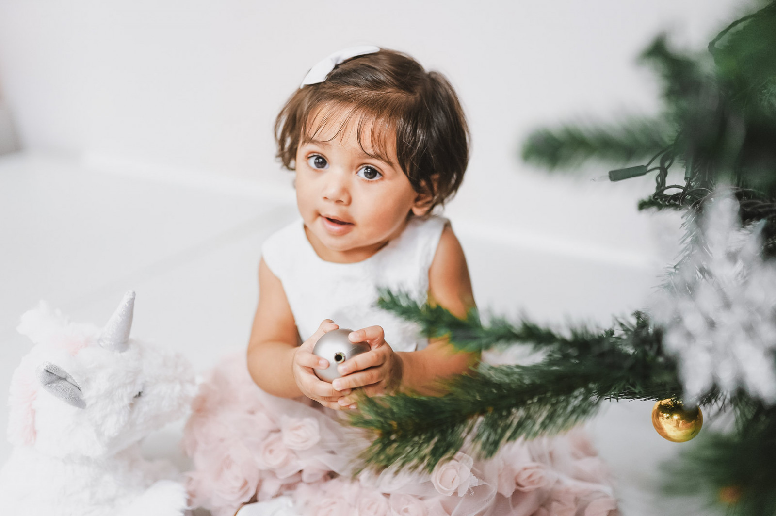 little baby girl sits next to christmas tree